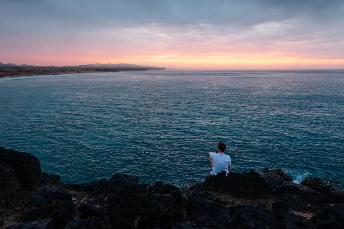 Sunrise on Fuerteventura: someone sits on dark rocks above the sea.
