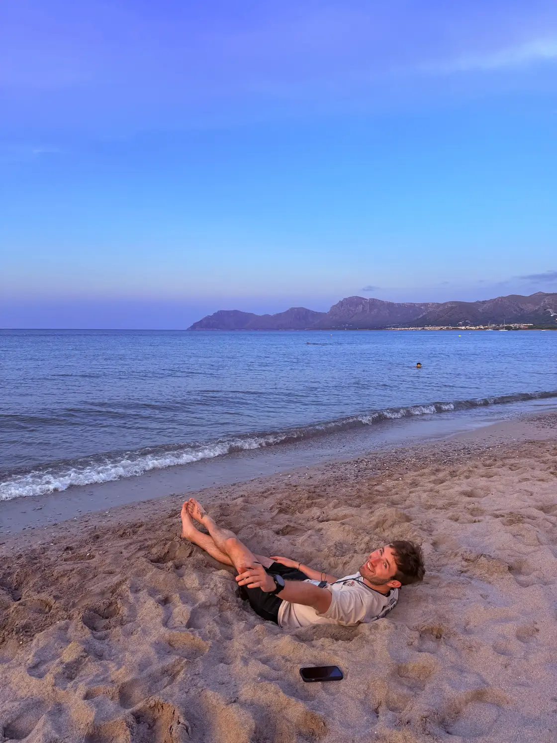 Lying on the beach after a spontaneous flight, with the sea and mountains in the evening light behind.
