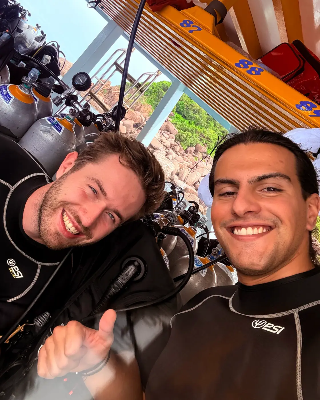 Two friends in wetsuits laughing on a dive boat in Thailand.