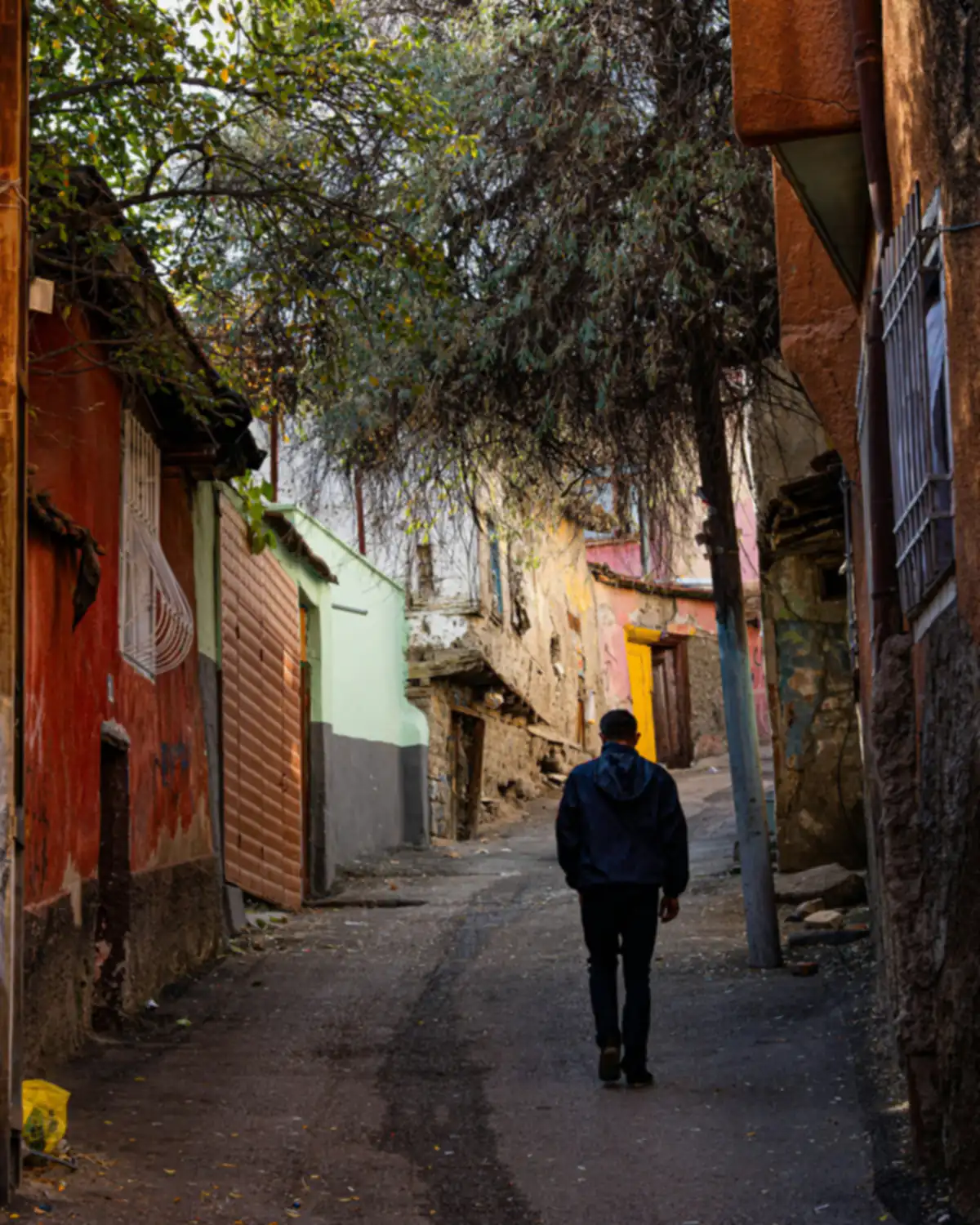 A person walks through a narrow old town lane in the morning, sun on the facades