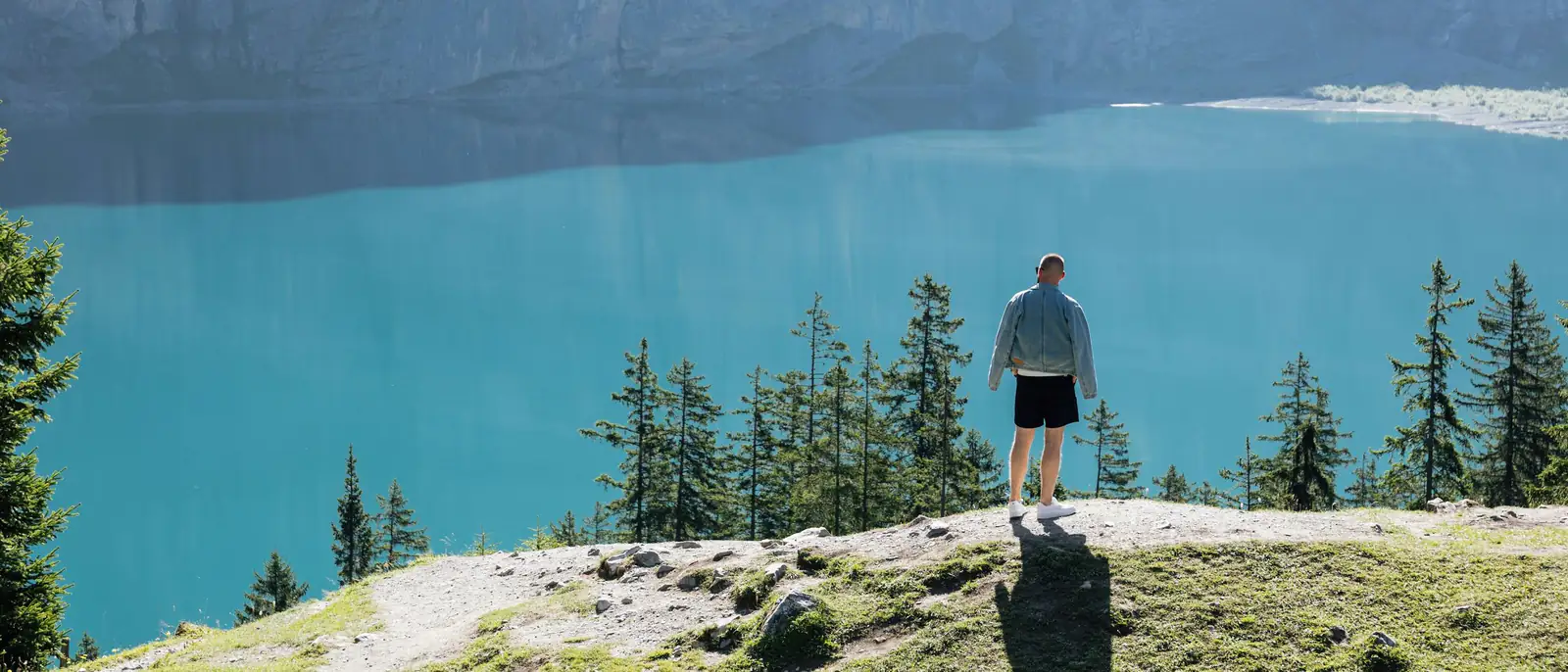 Eine Frau steht von hinten gesehen an einem Aussichtspunkt über einem See mit kleiner Stadt