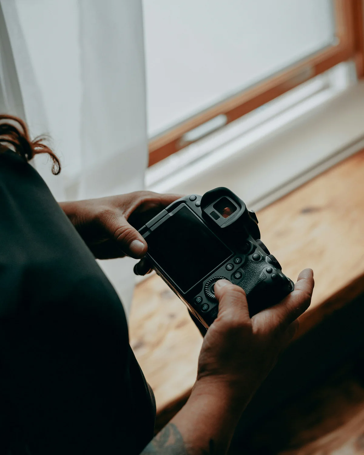 Hände halten eine Kamera und fotografieren ein helles Zimmer mit Bett und Fenster