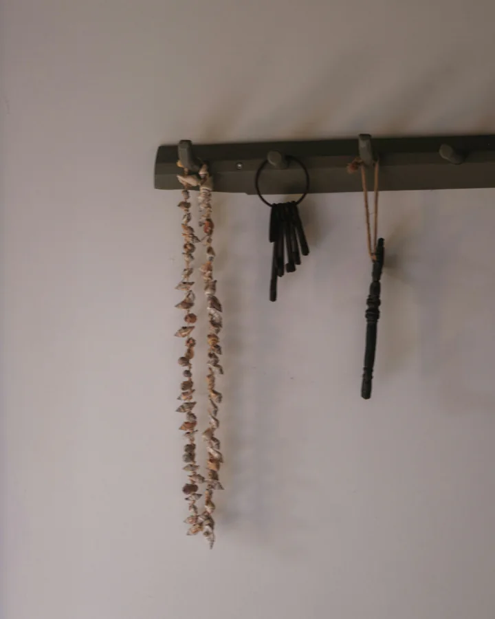 Schlüsselbrett an einer hellen Wand mit einem Schlüsselbund, einem alten Schlüssel und einer Muschelkette